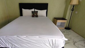 Un lit bien fait, recouvert d’une couvre-lit blanche et agrémenté d’oreillers, une table de chevet avec une lampe et une lampe sur pied dans une chambre d’hôtel.
