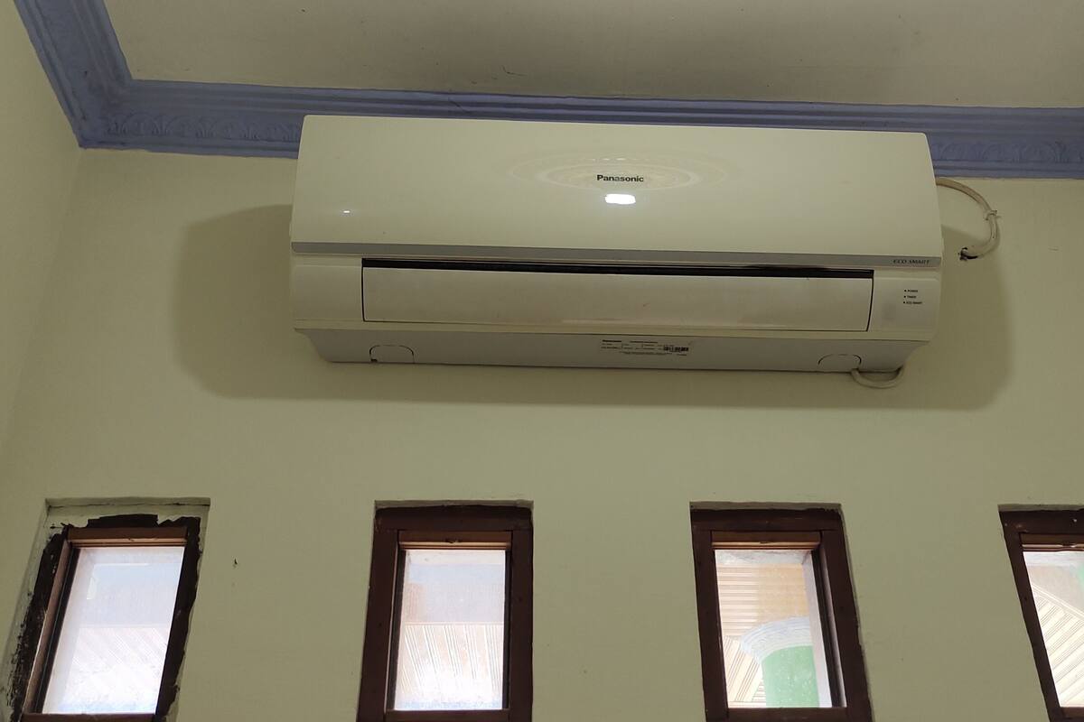 Une pièce dotée d’un climatiseur fixé au plafond, de trois fenêtres à cadre en bois et d’un plafond peint en bleu clair.