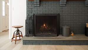 A fireplace with a fire, a wooden stool, and a metal shelf above it. - Green Sanctuary: Luxury Home Surrounded by Nature (New Paltz)