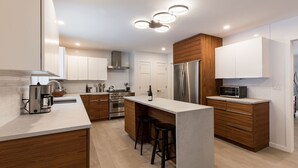 A modern kitchen with a central island, stainless steel appliances, wooden cabinets, and a built-in microwave. - Green Sanctuary: Luxury Home Surrounded by Nature (New Paltz)