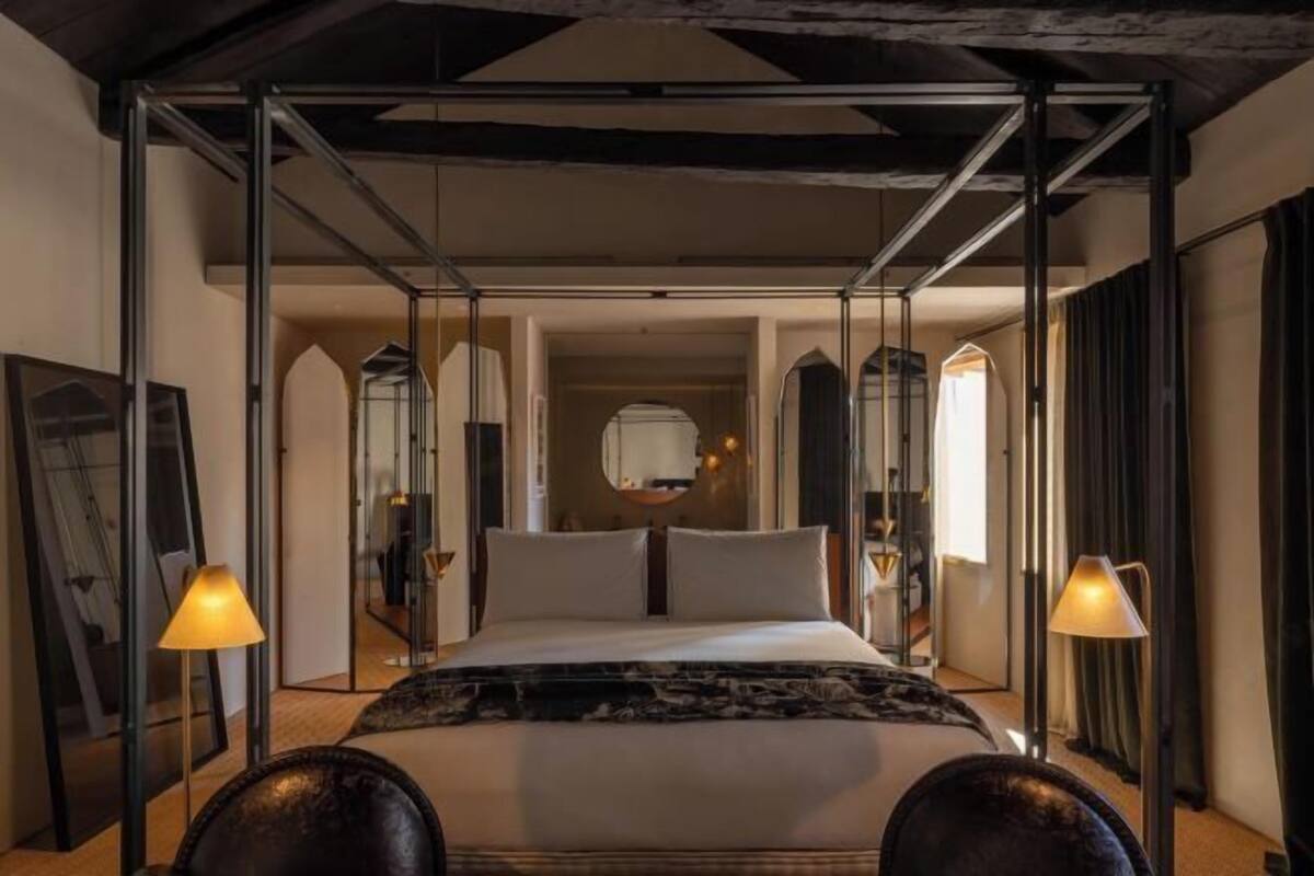Een kamer met een bed, twee lampen, een spiegel en uitzicht op een gang.