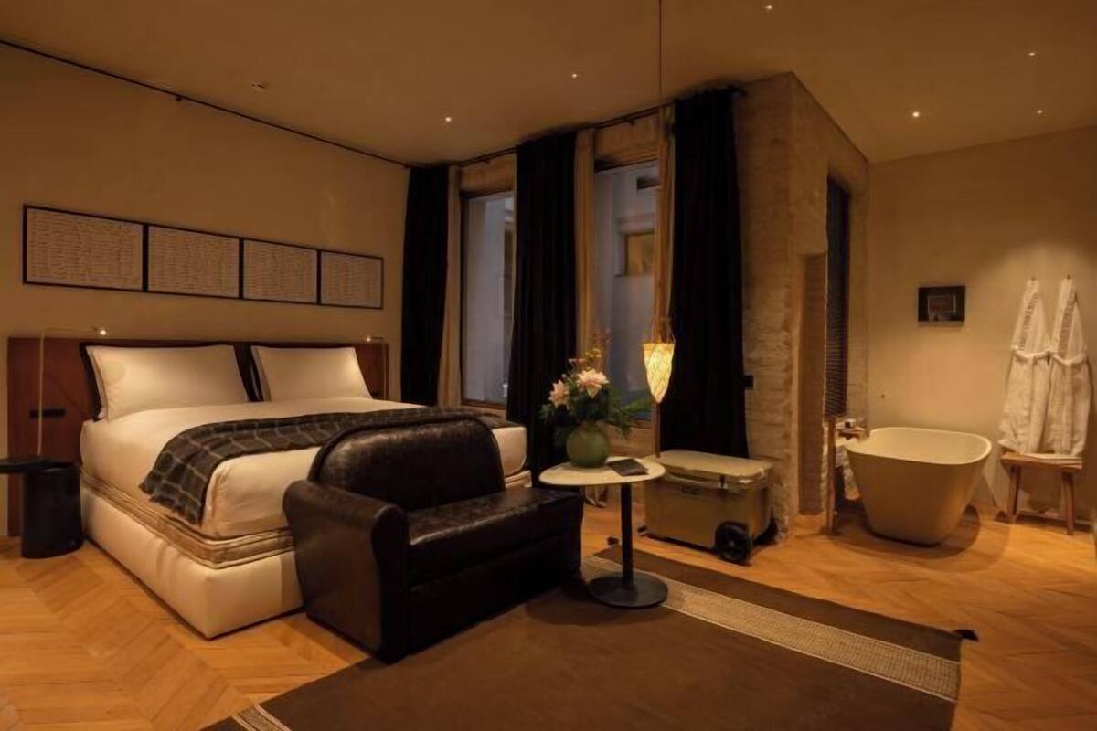 Hotelkamer met een bed, een slaapbank, een tafeltje, een lamp, een badkuip en een spiegel.