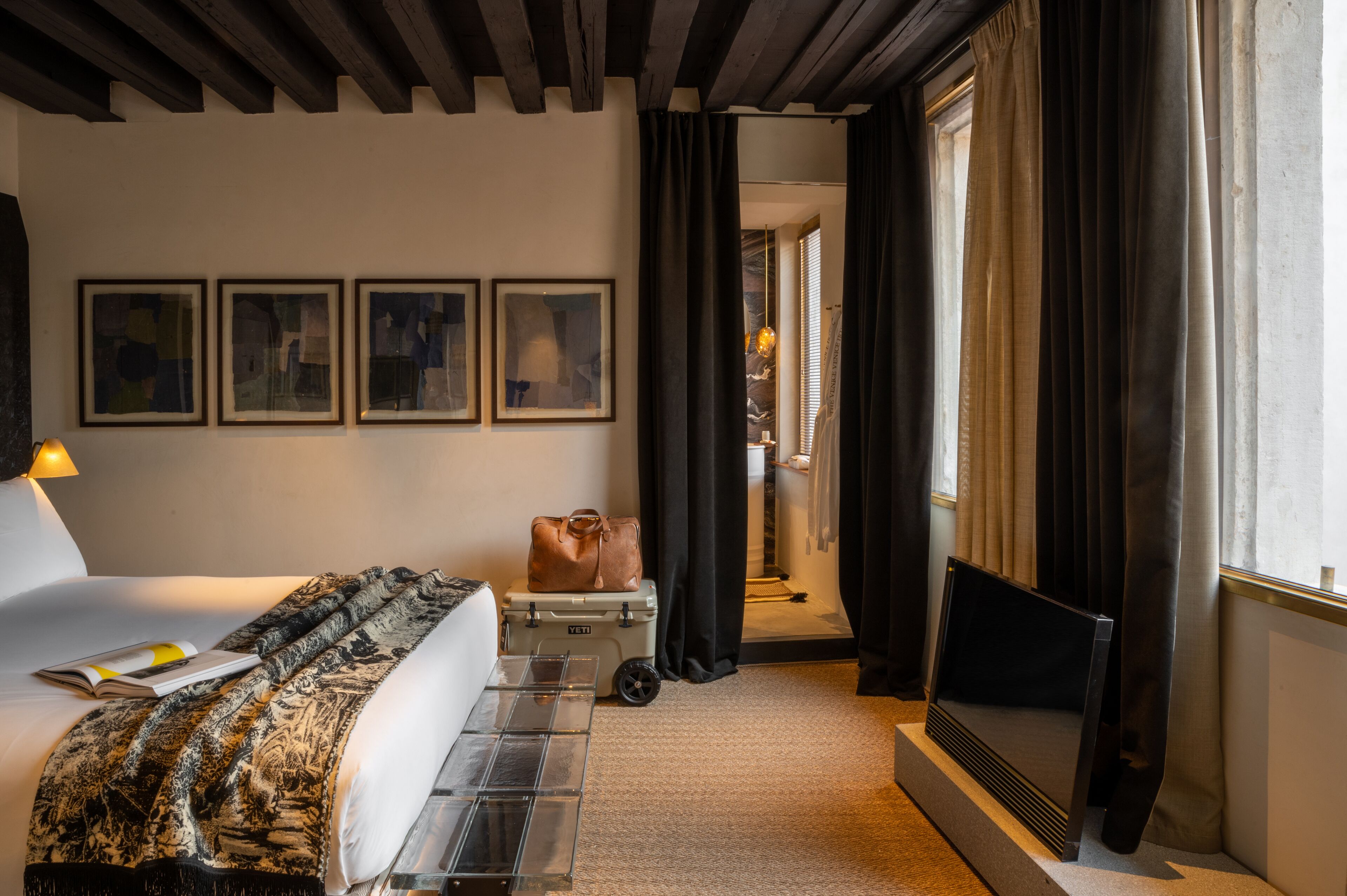 Una habitación de hotel con cama, televisión, maleta y ventana con cortinas.