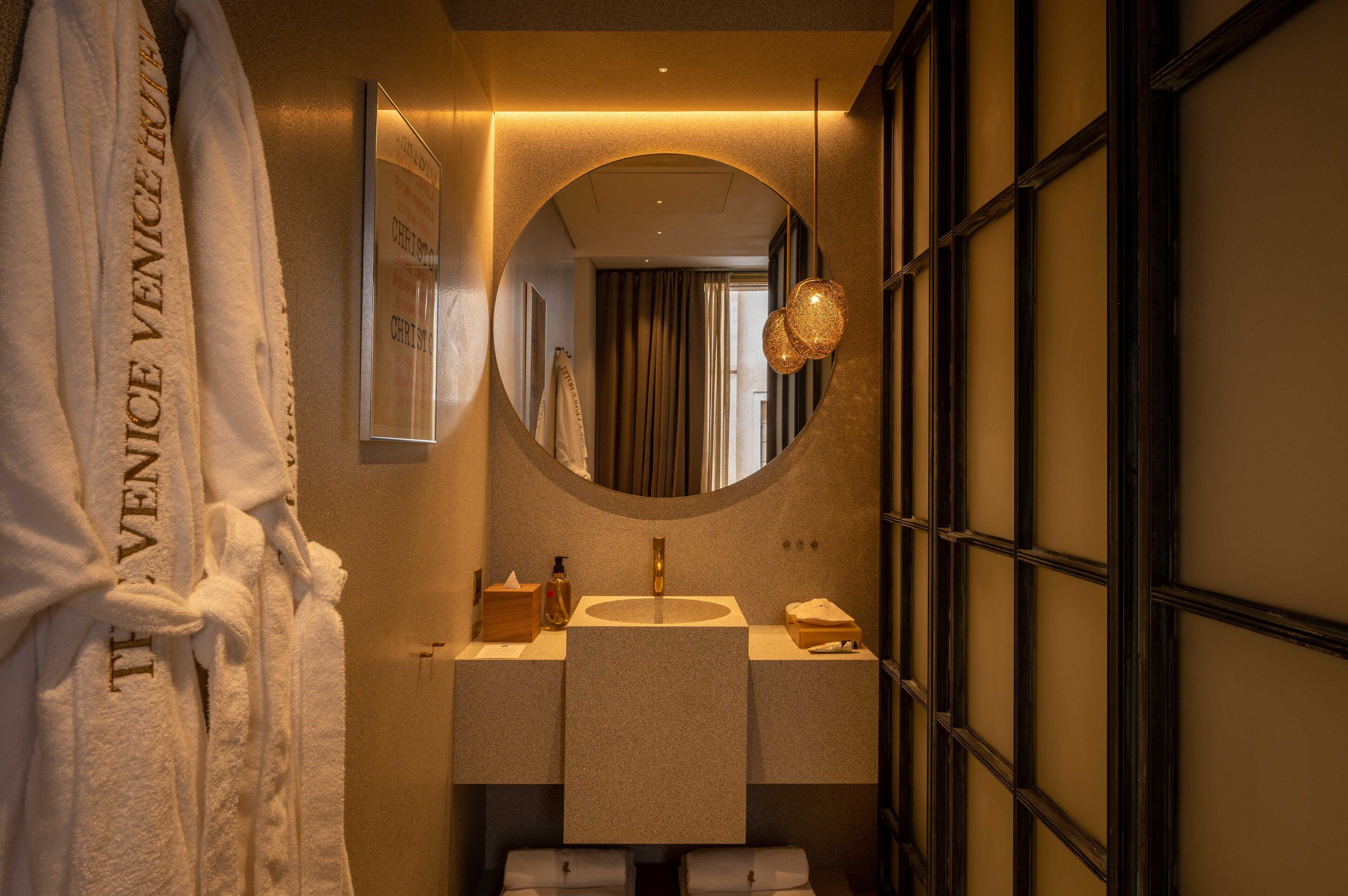 Un bagno con uno specchio tondo, un lavandino e un porta asciugamani con accappatoi.