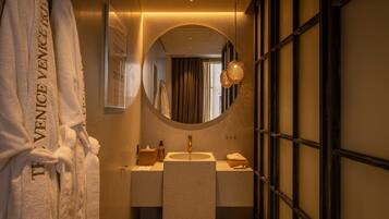 Un bagno con uno specchio tondo, un lavandino e un porta asciugamani con accappatoi.