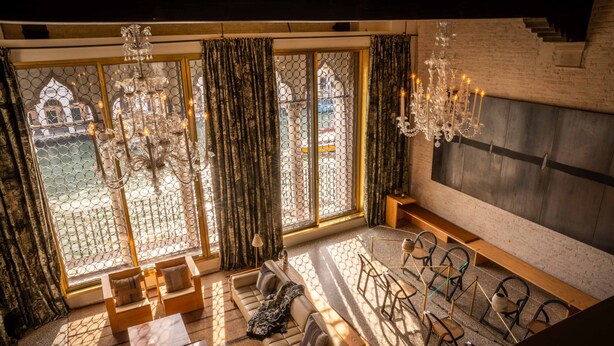 A spacious room with a large window, a sofa, a coffee table, and a chandelier. - The Venice Venice Hotel (Venice)