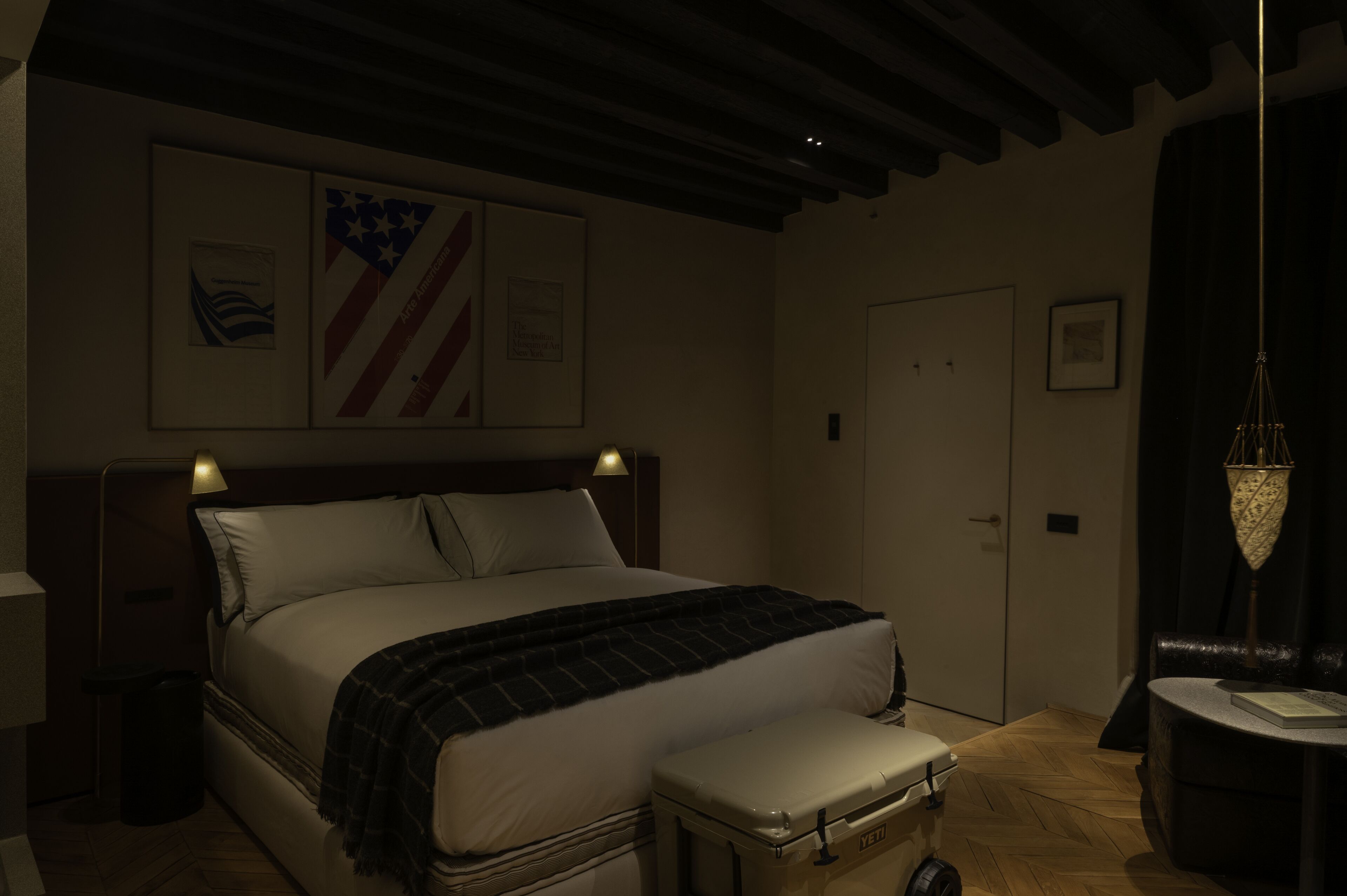 A dimly lit hotel room with a large bed, a suitcase, and a wall with framed pictures.