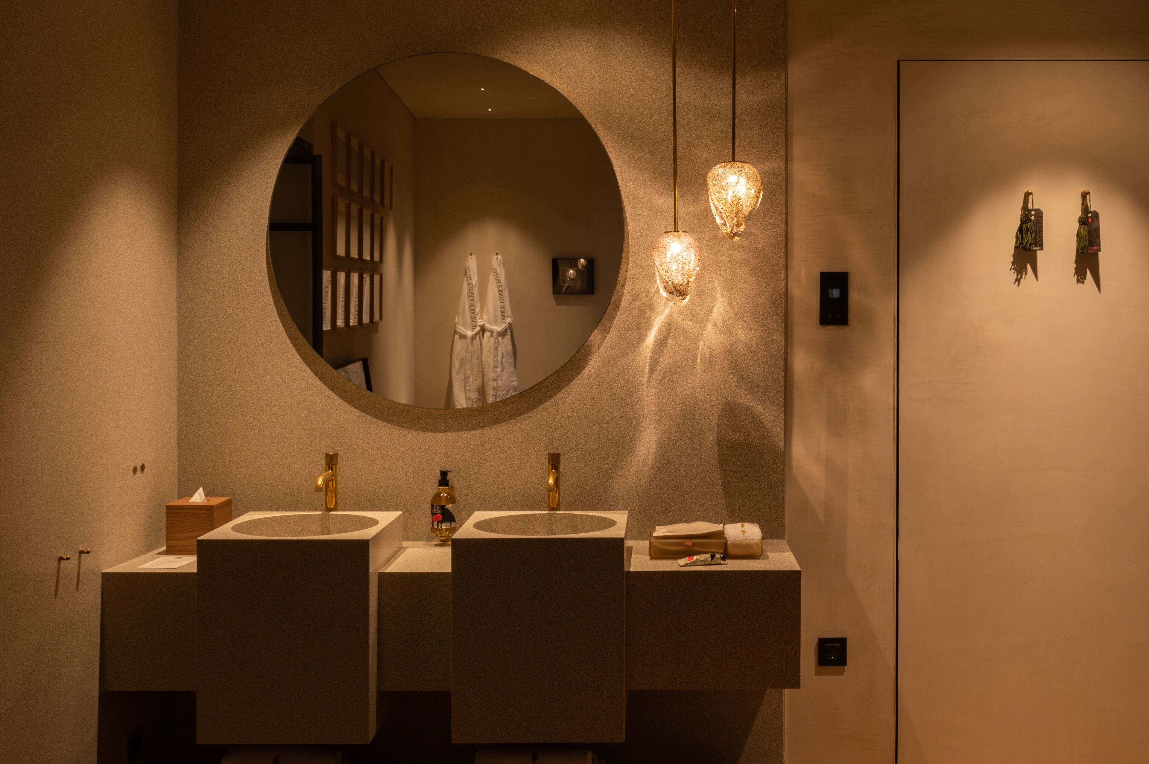 Un bagno moderno con tre lavandini, uno specchio grande e luci a sospensione.