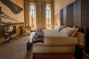 Ein modernes Hotelzimmer mit einem großen Bett, einem Flachbildfernseher, einem Kamin und Blick auf die Stadt durch große Fenster.