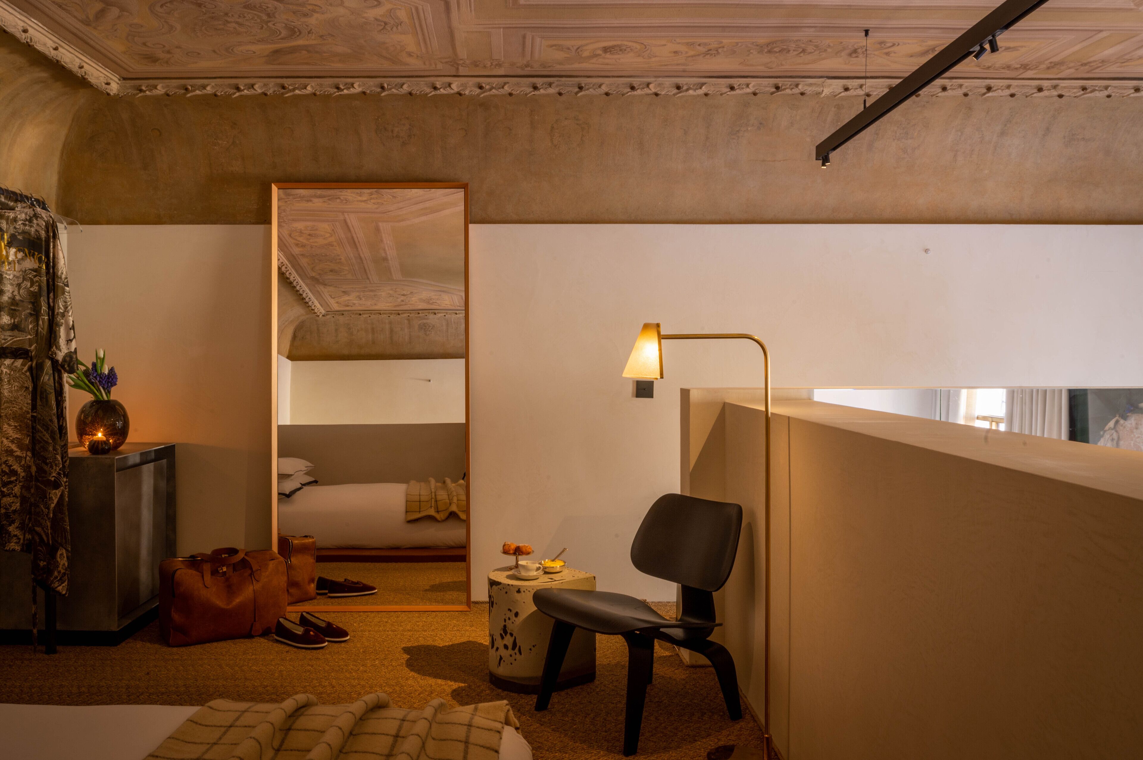 Une chambre d’hôtel avec un lit, une chaise, une lampe, une petite table et une valise.