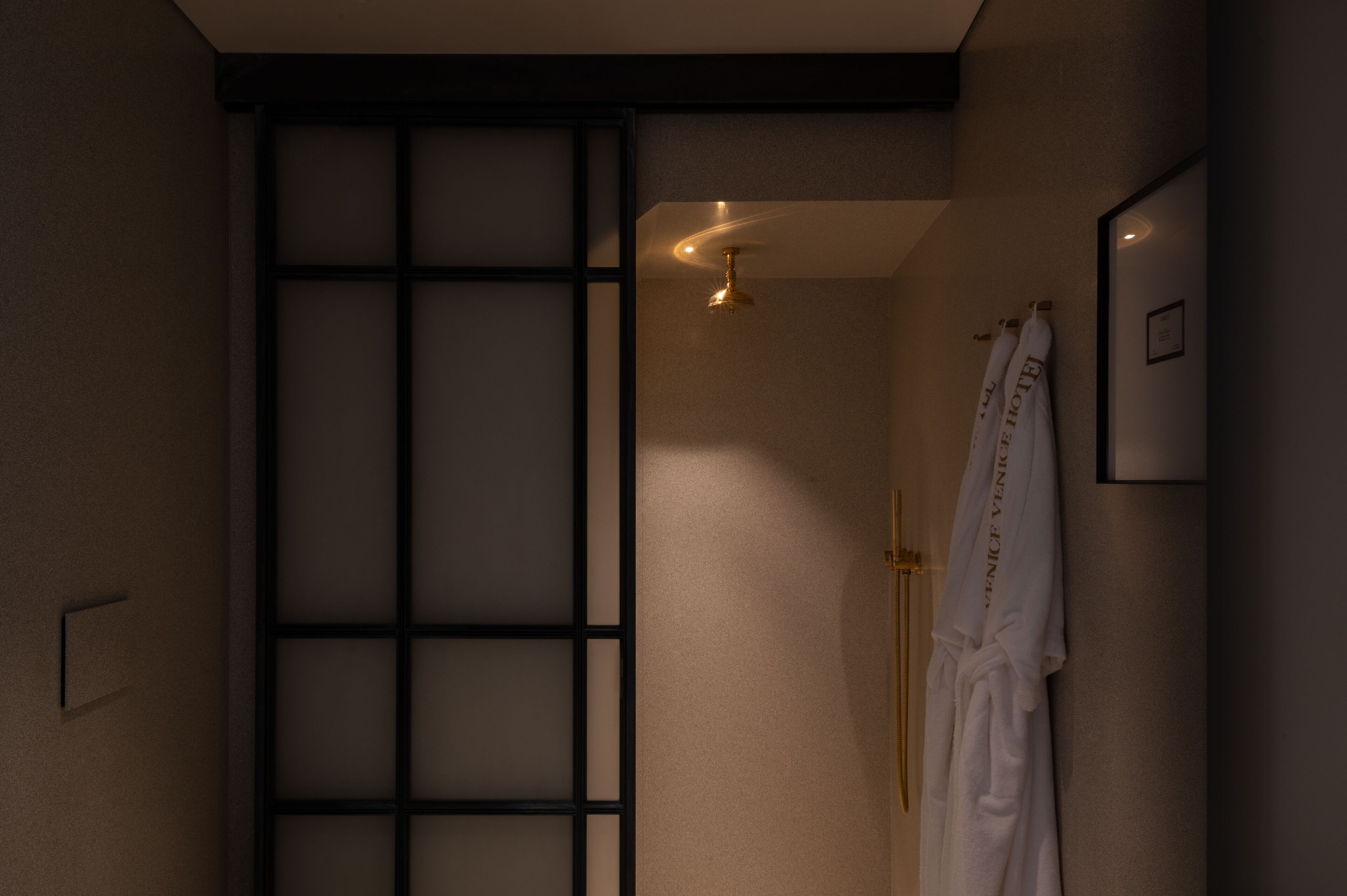 A modern bathroom with a sliding door, a towel rack with robes, and a ceiling light fixture.