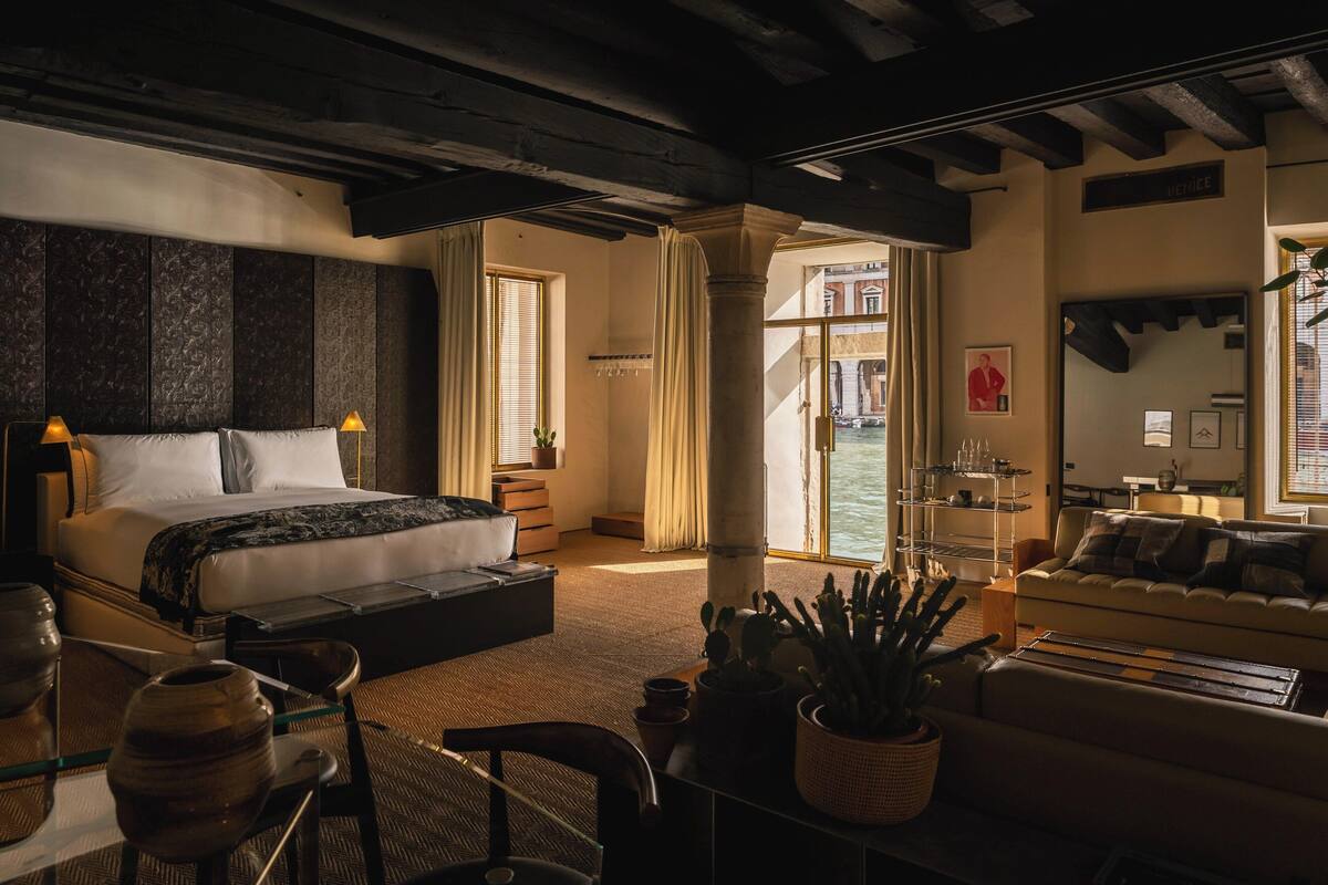 Een ruime slaapkamer met een groot bed, een zithoek met een bank en uitzicht op een binnenplaats.