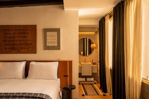 Quarto de hotel com uma cama, mesa de cabeceira, espelho, pia e cortinas.