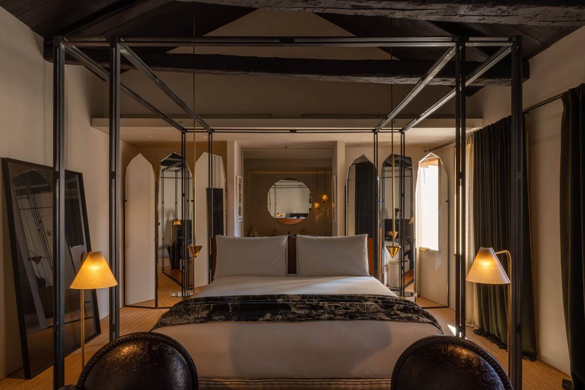 Een moderne hotelkamer met een groot bed, twee bedlampjes en een spiegel boven het bed.