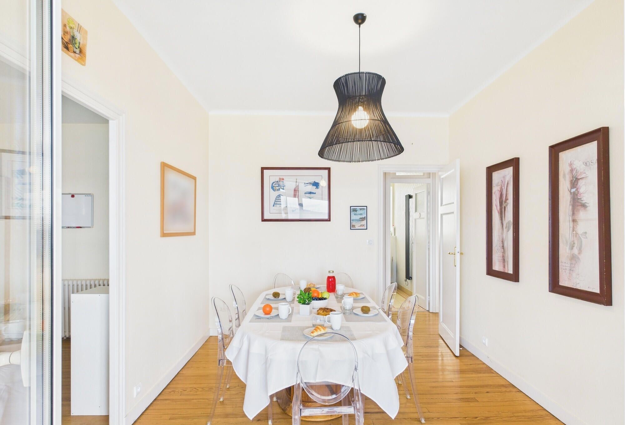 A dining area with a table set for four, a hanging light fixture, and framed artwork on the walls.
