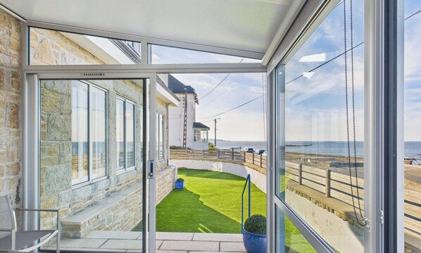 A conservatory with a view of the sea, stone walls, and a grassy area.