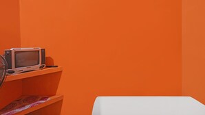 A room with a television on a shelf, a white table, and orange walls. - Hotel O Penginapan ReniNearMall Nagoya Hill (Batam)