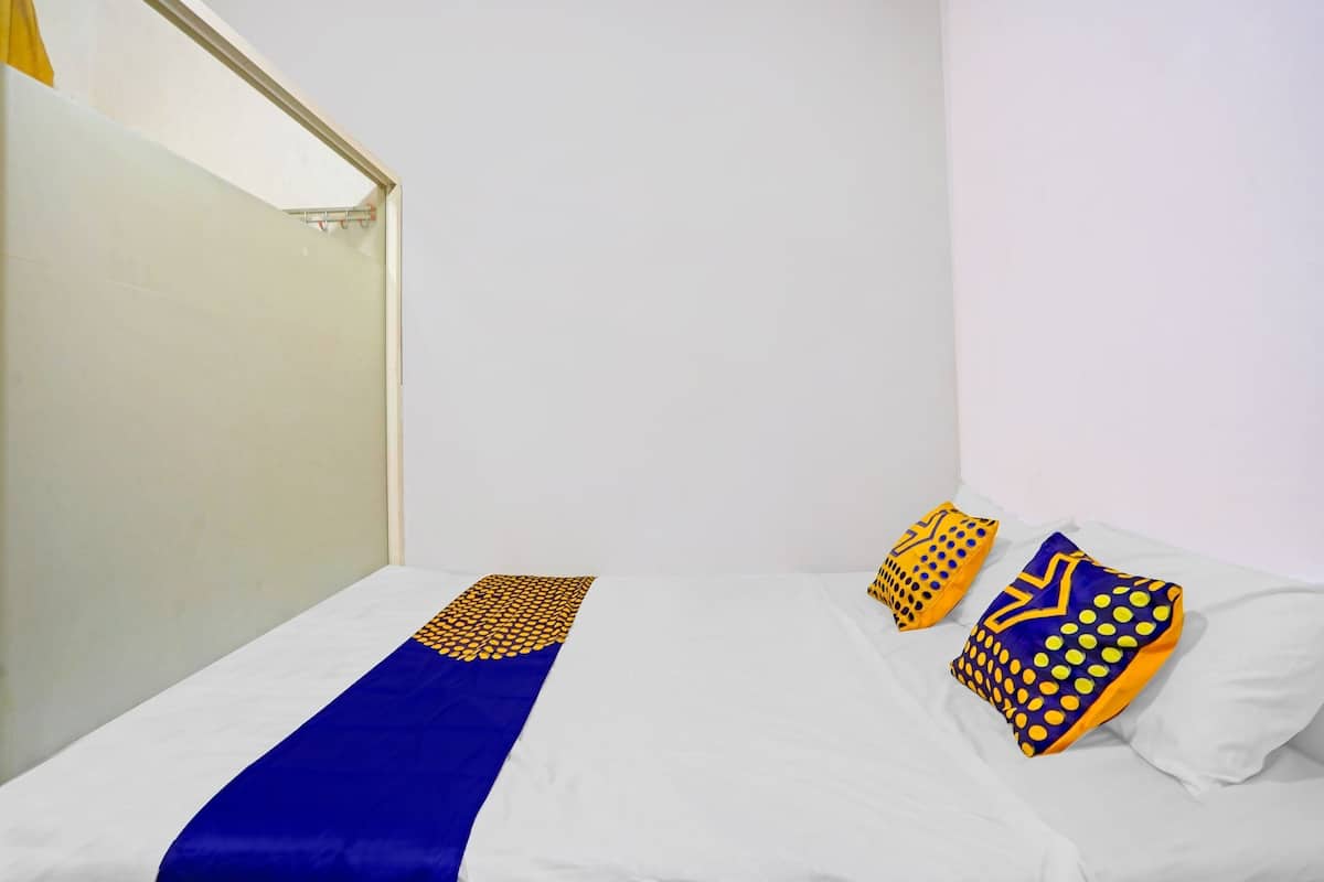 A single bed with a blue and yellow bedspread, two patterned pillows, and a white wall.