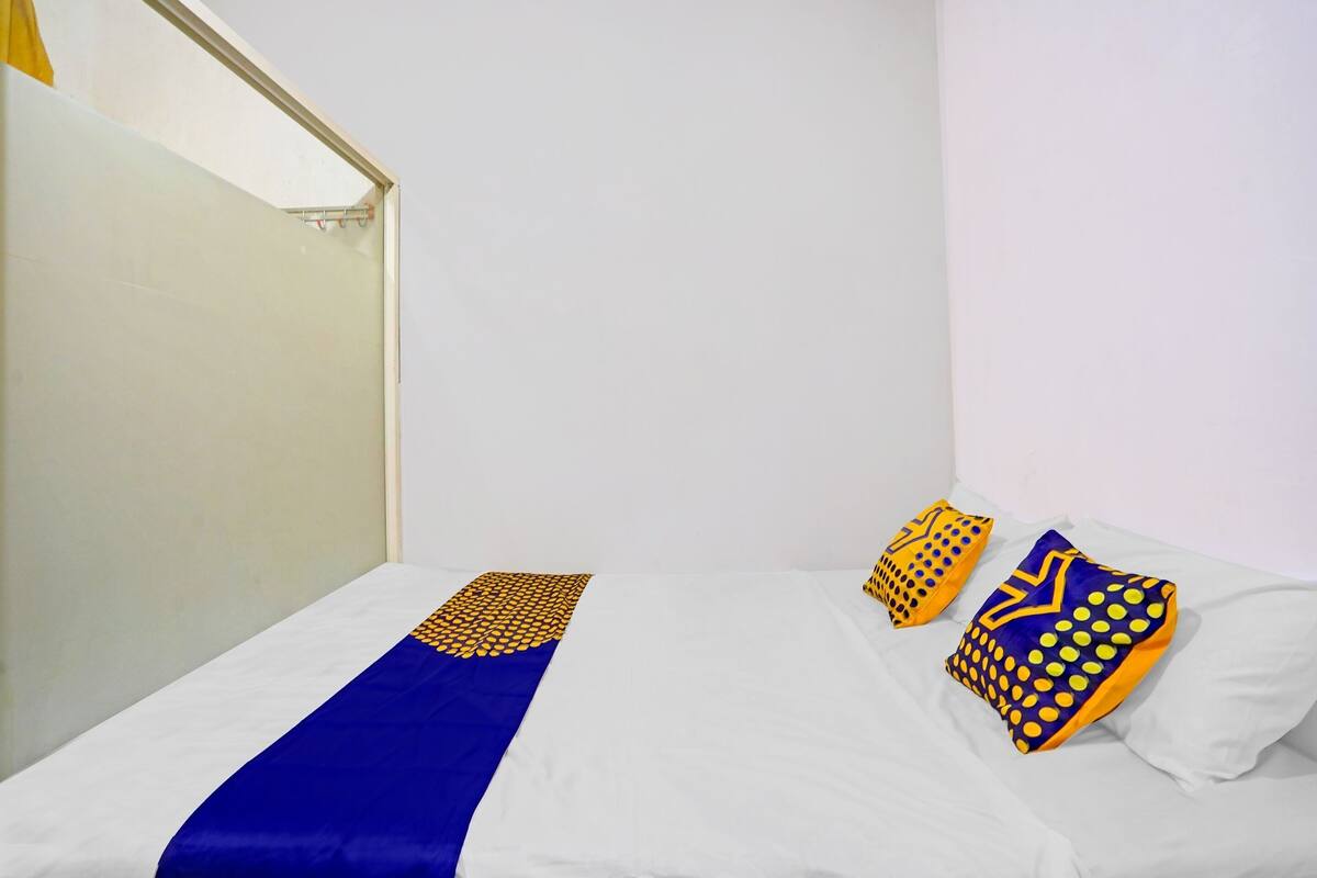 A single bed with a blue and yellow bedspread, two patterned pillows, and a white wall.
