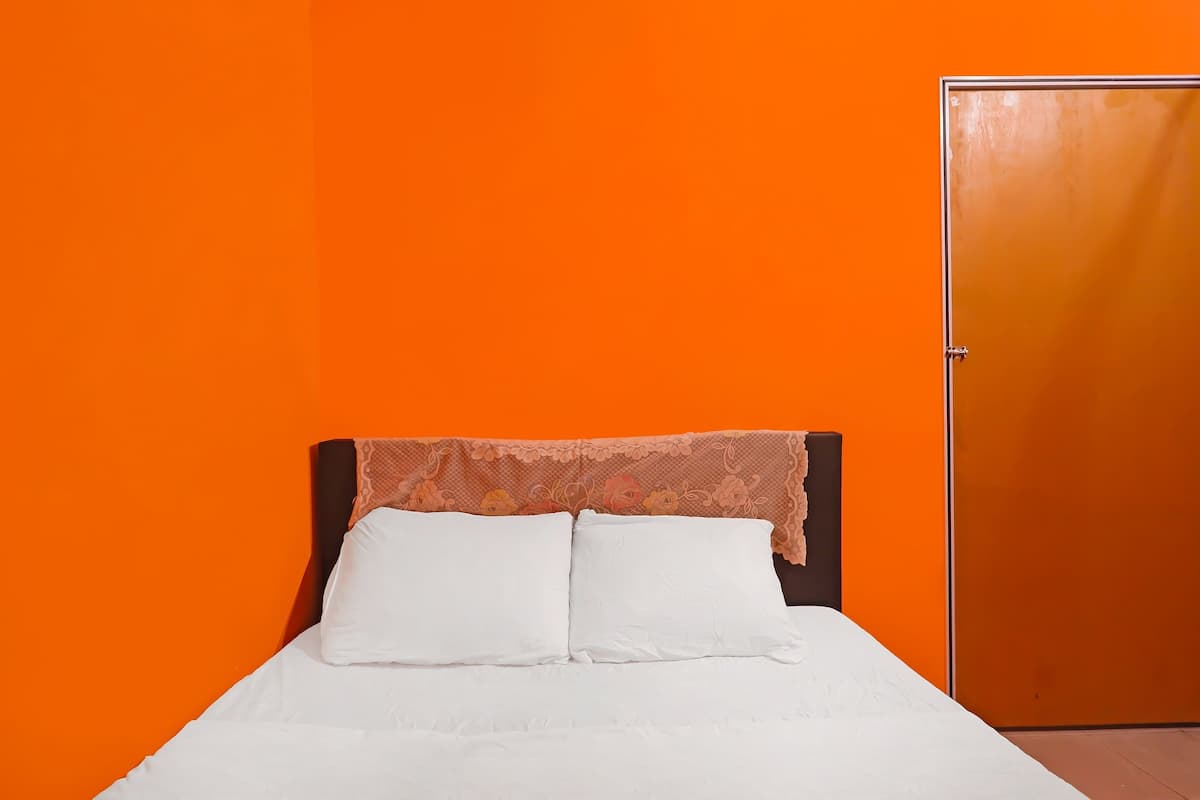 A bed with white bedding in a room with orange walls and a wooden door.