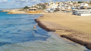 A coastal town with clear waters, a sandy beach, and buildings in the background. - Apartment with the most beautiful sunset in Sicily (Frazione Cava d'Aliga, Scicli)
