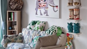 A living room with a sofa, decorative pillows, a wall-mounted air conditioner, a bookshelf, and a framed elephant artwork. - Apartment with the most beautiful sunset in Sicily (Frazione Cava d'Aliga, Scicli)