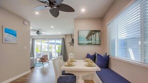 A dining area with a table set for four, a bench with cushions, a ceiling fan, and a large window with blinds.