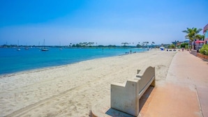 A beach with a sandy shore, a concrete bench, and a clear blue sky.
