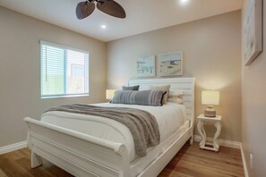 A bedroom with a white bed, a ceiling fan, a bedside table with a lamp, and two wall-mounted pictures. - 2 Houses to Beach * Exclusive Patio * Dog OK (San Diego)