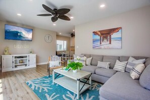 A living room with a TV, ceiling fan, and artwork depicting a beach scene. - 2 Houses to Beach * Exclusive Patio * Dog OK (San Diego)