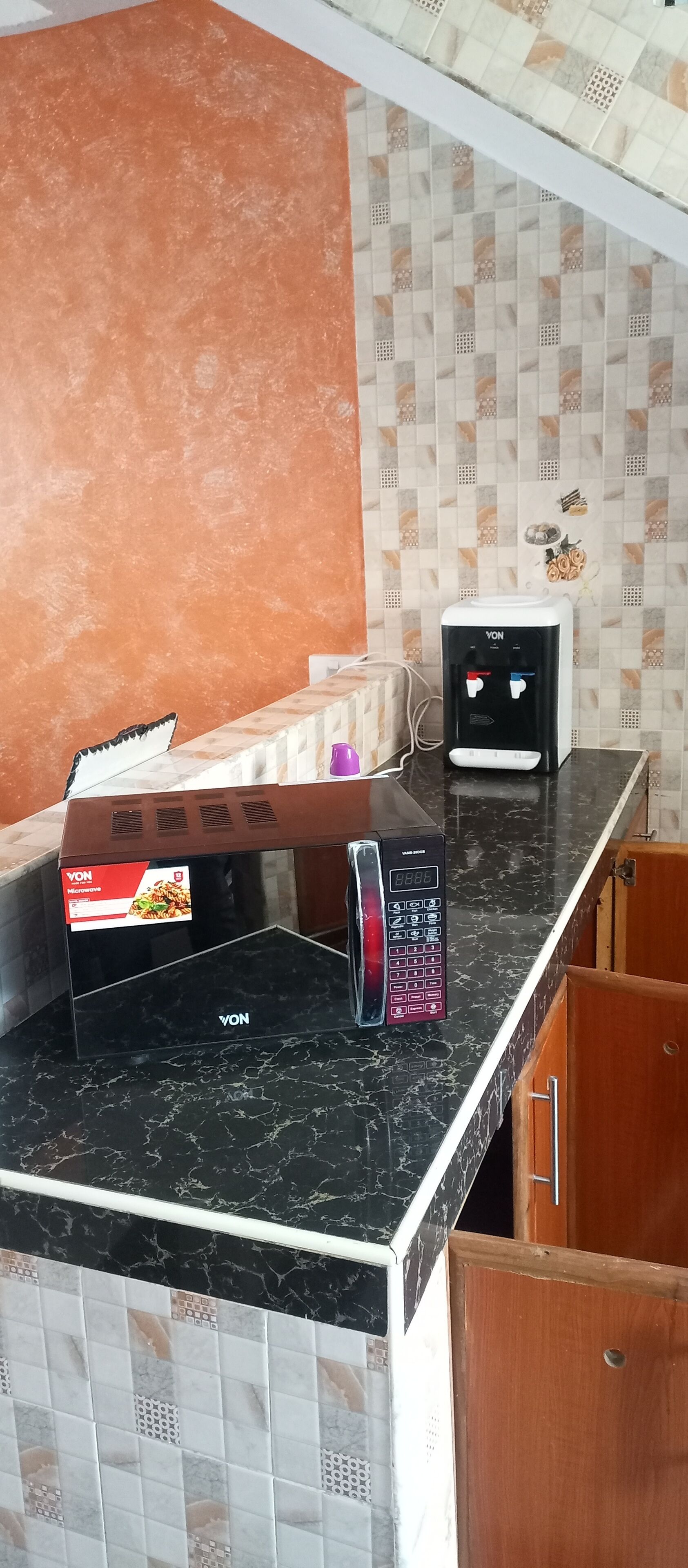 A kitchen with a microwave, a water dispenser, and a tiled backsplash.