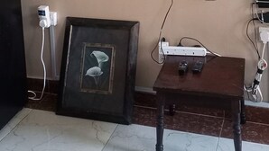 Ein Wohnzimmer mit einem wandmontierten Flachbildfernseher, einem gerahmten Bild an der Wand, einem kleinen Holztisch und einer weißen Steckdose.