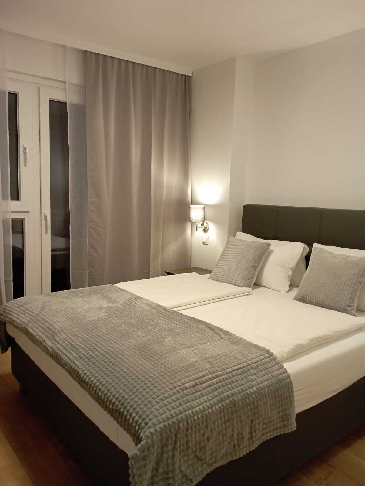 A neatly made bed with a grey blanket, a wall-mounted light, and a dark headboard.
