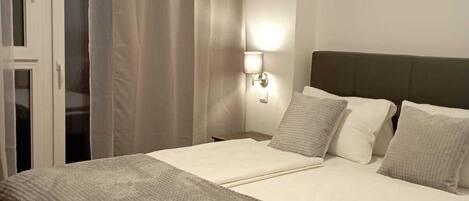 A neatly made bed with a grey blanket, a wall-mounted light, and a dark headboard.