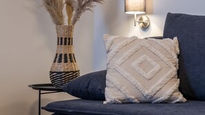 A modern living room with a dark sofa, a woven vase with pampas grass, and a wall-mounted lamp. - Hotel Fuchs und Hase (Rosegg)