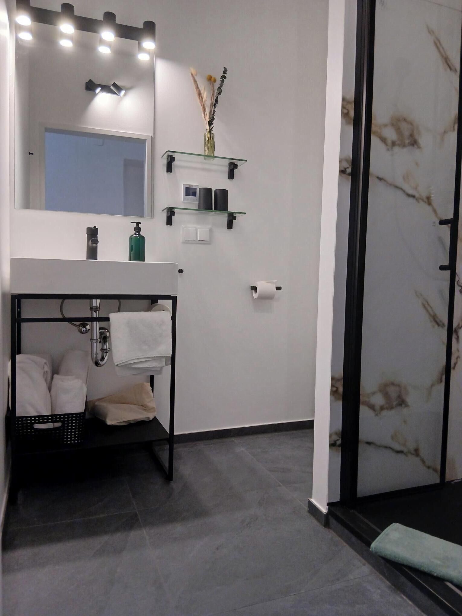 A modern bathroom with a vanity, mirror, towel rack, and a shower area.