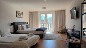 A modern hotel room with two beds, a desk, a chair, a TV, and a balcony with curtains. - Hotel Fuchs und Hase (Rosegg)
