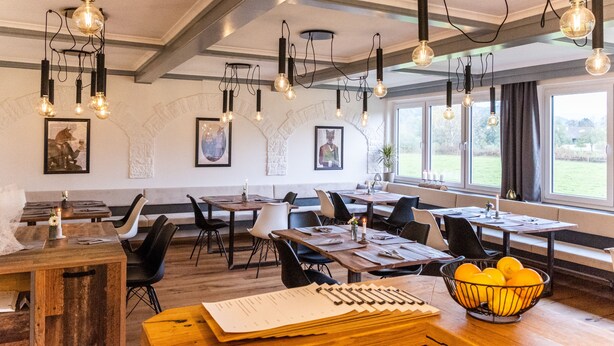 A restaurant with wooden tables, black chairs, and hanging light fixtures. - Hotel Fuchs und Hase (Rosegg)