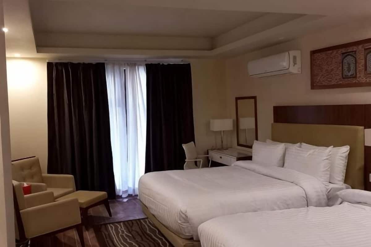 A hotel room with two beds, a desk, a chair, and an air conditioning unit.