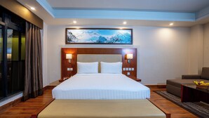 A hotel room with a large bed, two bedside lamps, a painting above the bed, a sofa, and a small table with fruit.