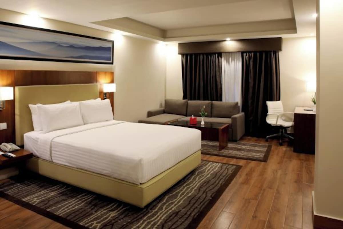 Una habitación de hotel con una cama grande, un sofá, un escritorio y una ventana con cortinas.