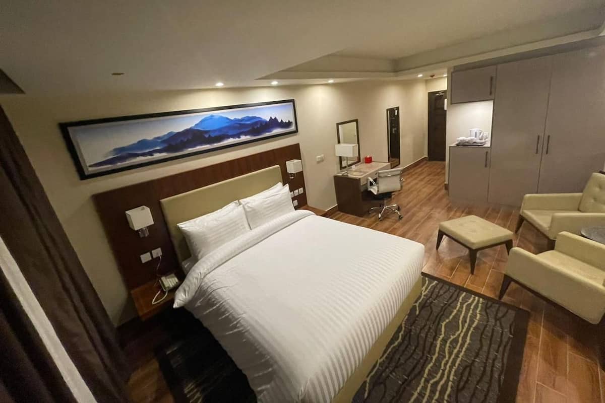A hotel room with a large bed, a desk with a chair, a wardrobe, and a painting on the wall.