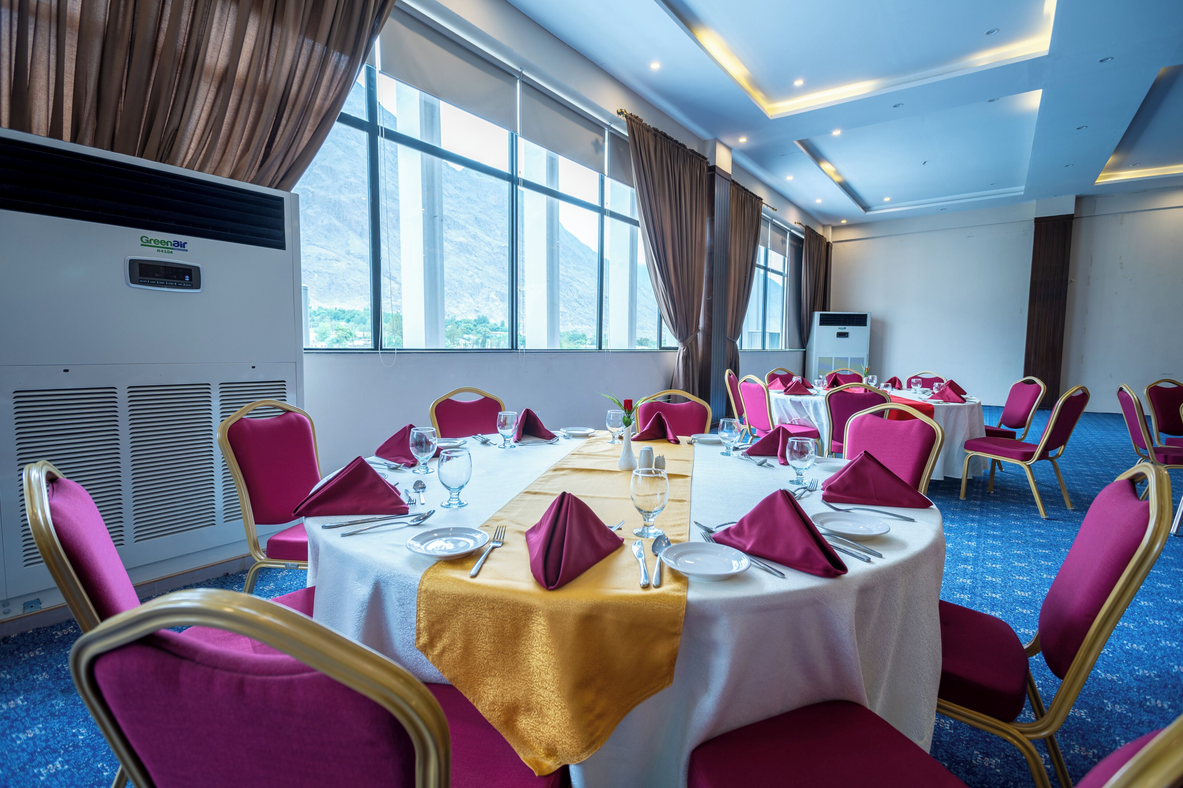 Un salón de conferencias con mesas redondas, sillas rojas y vistas a montañas a través de amplios ventanales.