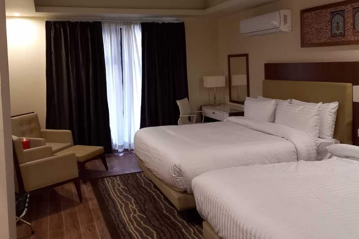 A hotel room with two beds, a desk, a chair, and a large window with curtains.