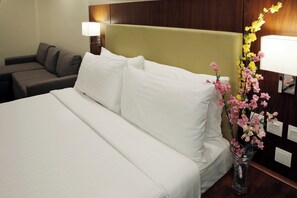 A hotel room with a bed, a sofa, a nightstand with a lamp, and a vase with flowers. - Avari Xpress Gilgit (Gilgit)
