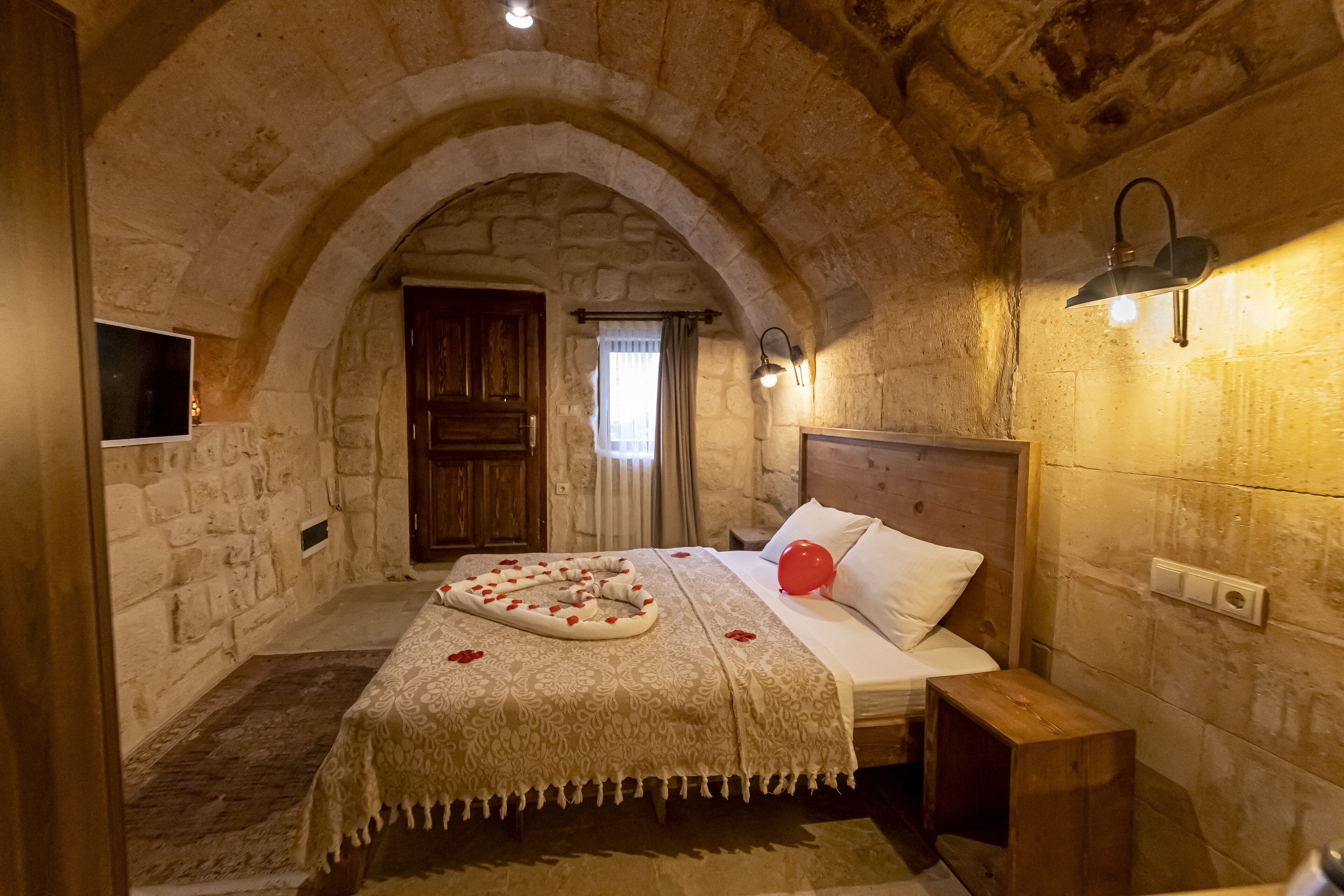 A cozy room with a stone archway, a bed with a heart-shaped decoration, and a nightstand.