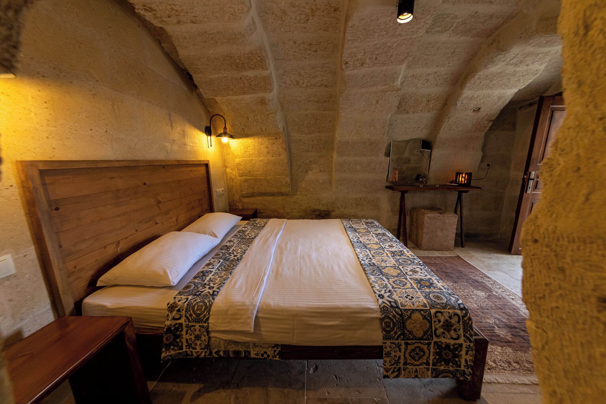 A rustic room with a wooden bed, a patterned rug, and a stone ceiling.