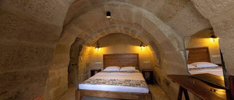 Un dormitorio con paredes de piedra, una cama de madera, dos mesitas de noche y un espejo.
