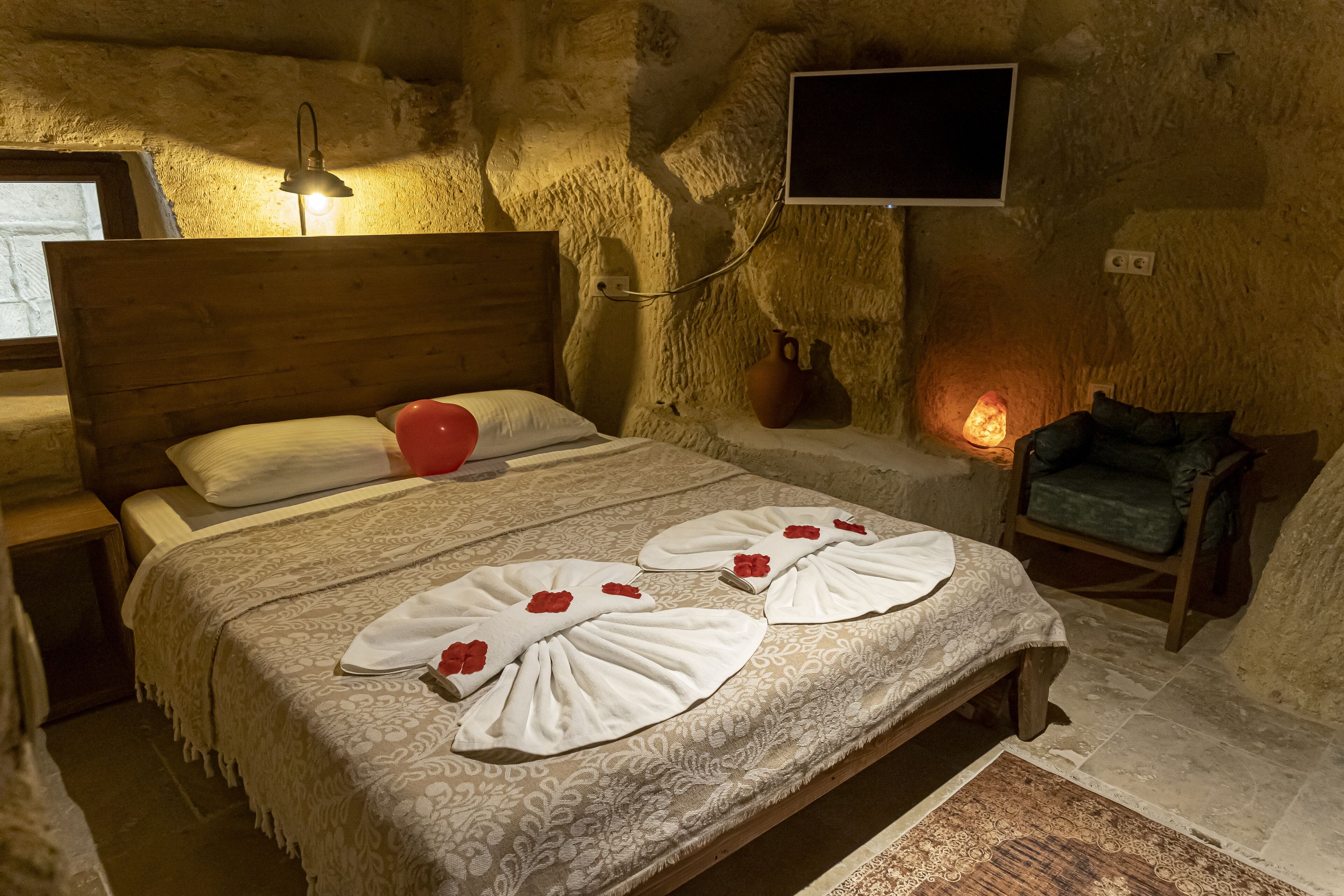 Un dormitorio acogedor con una cama de madera, una lámpara de noche, un televisor de pantalla plana y una pared de piedra.