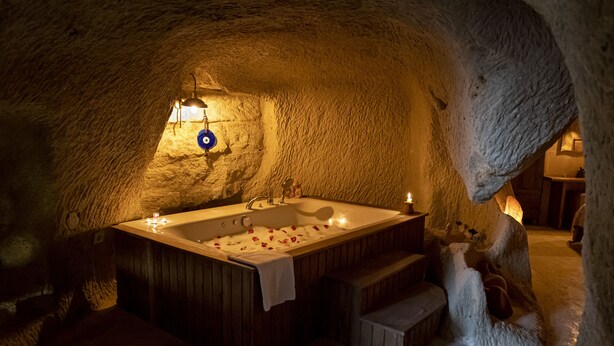 Une salle de bain aux murs de pierre, avec une baignoire en bois, un lavabo et un luminaire bleu.